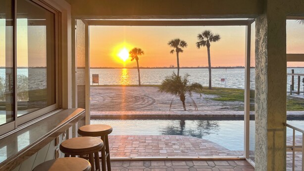 Een terras met honingraatmozaïek, uitzicht op de zonsondergang over het water, en palmbomen.