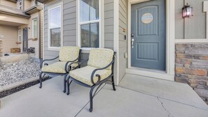 Een huis met een grijze deur, twee gestoffeerde stoelen ervoor en een stenen muur.