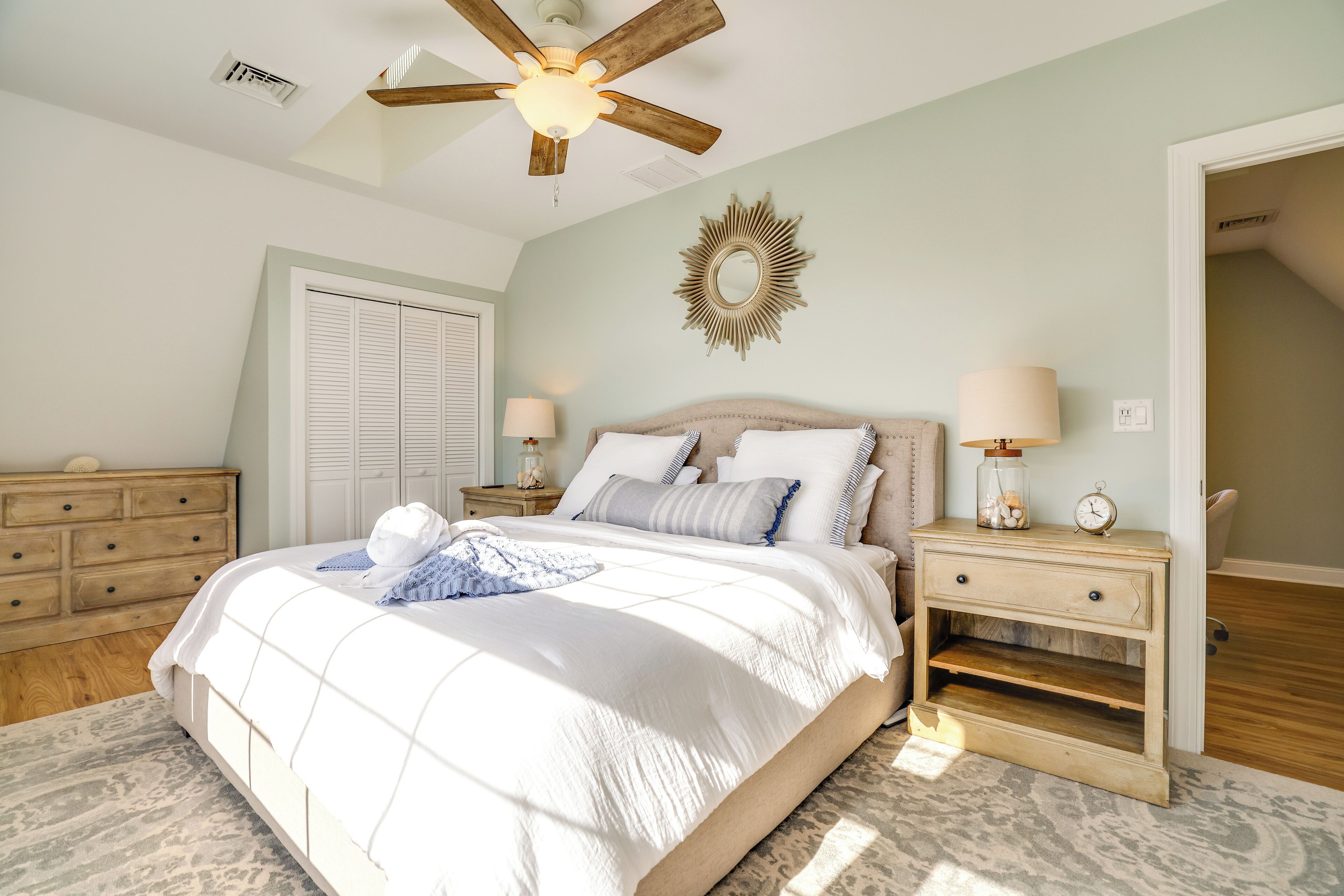 A bedroom with a bed, bedside tables, a ceiling fan, a mirror, and a door.