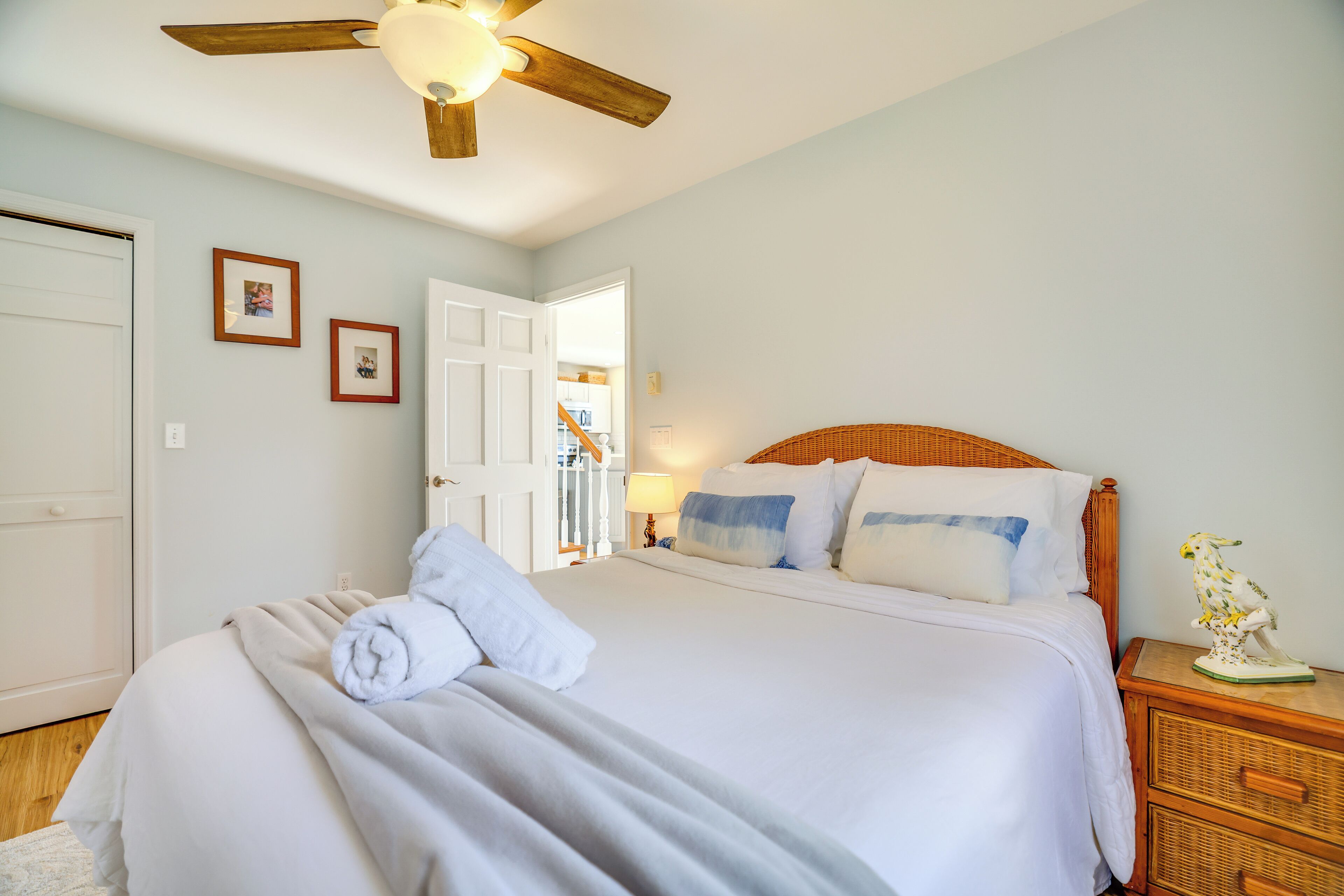 A bedroom with a bed, a wooden nightstand, a ceiling fan, and a door.