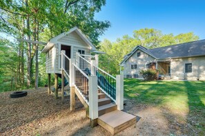 A wooden deck with a staircase leading to a house, surrounded by trees and a grassy yard. - Cow Shed Waterfront 3BR Home w/ Boat Dock! (Lancaster)