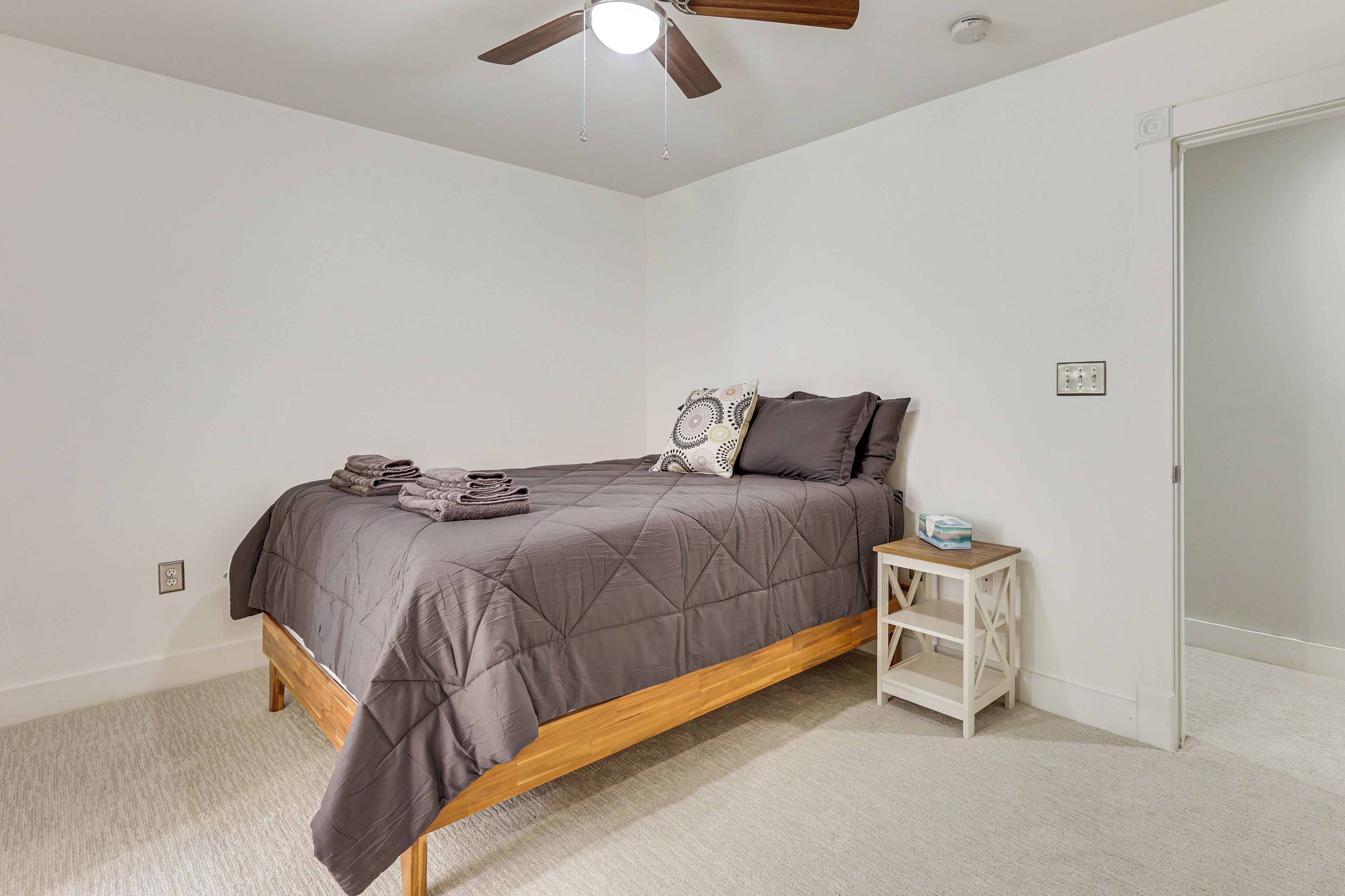 Un dormitorio con cama, mesita de noche, ventilador de techo y puerta.
