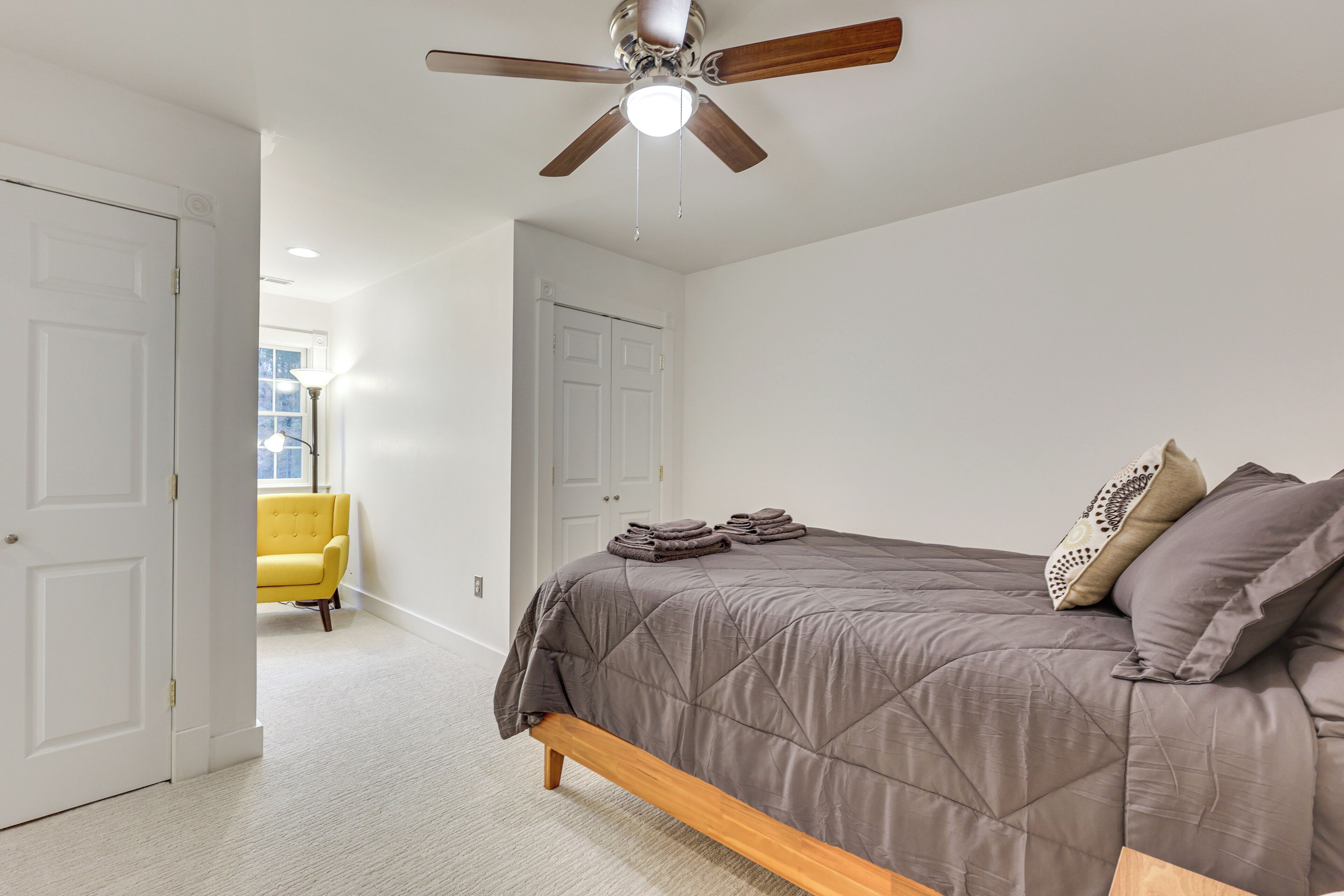 A bedroom with a bed, a ceiling fan, and a yellow chair in the background.