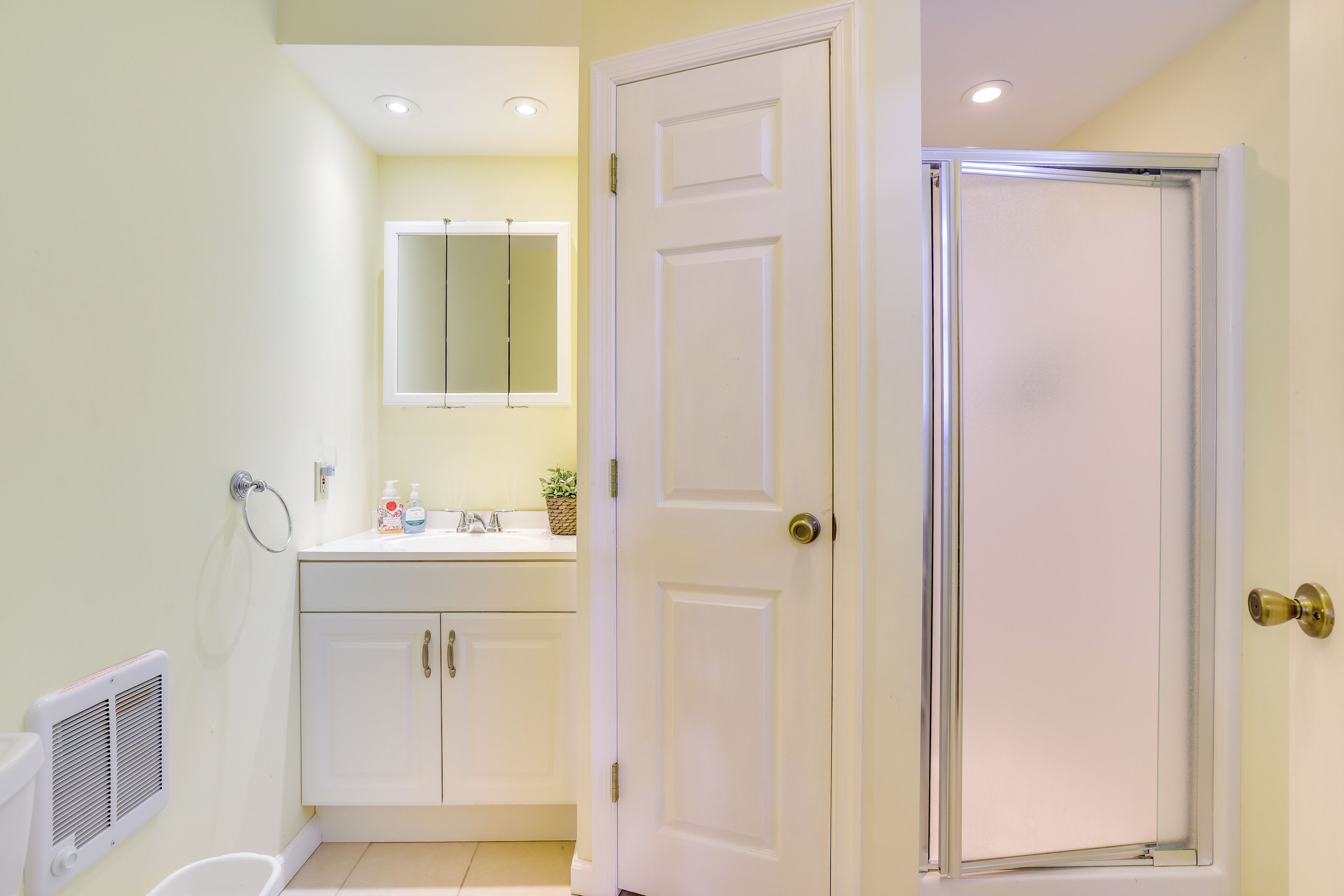 A bathroom with a white door, a sink, a mirror, and a shower area.