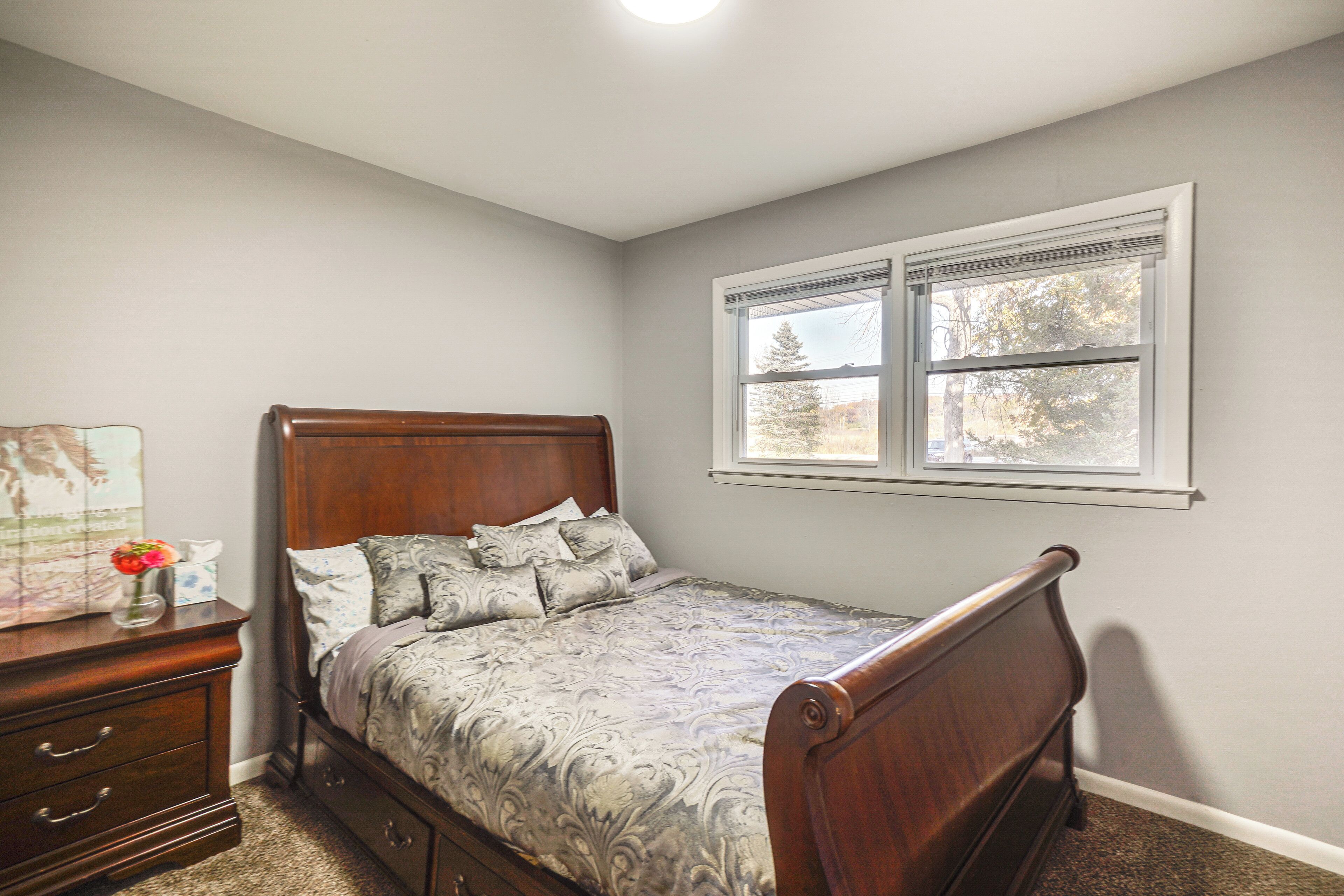 A bedroom with a wooden bed, a nightstand, and a window with blinds.