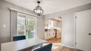 Cocina moderna con gabinetes blancos, un comedor con mesa y sillas, y vistas al exterior a través de amplias ventanas.