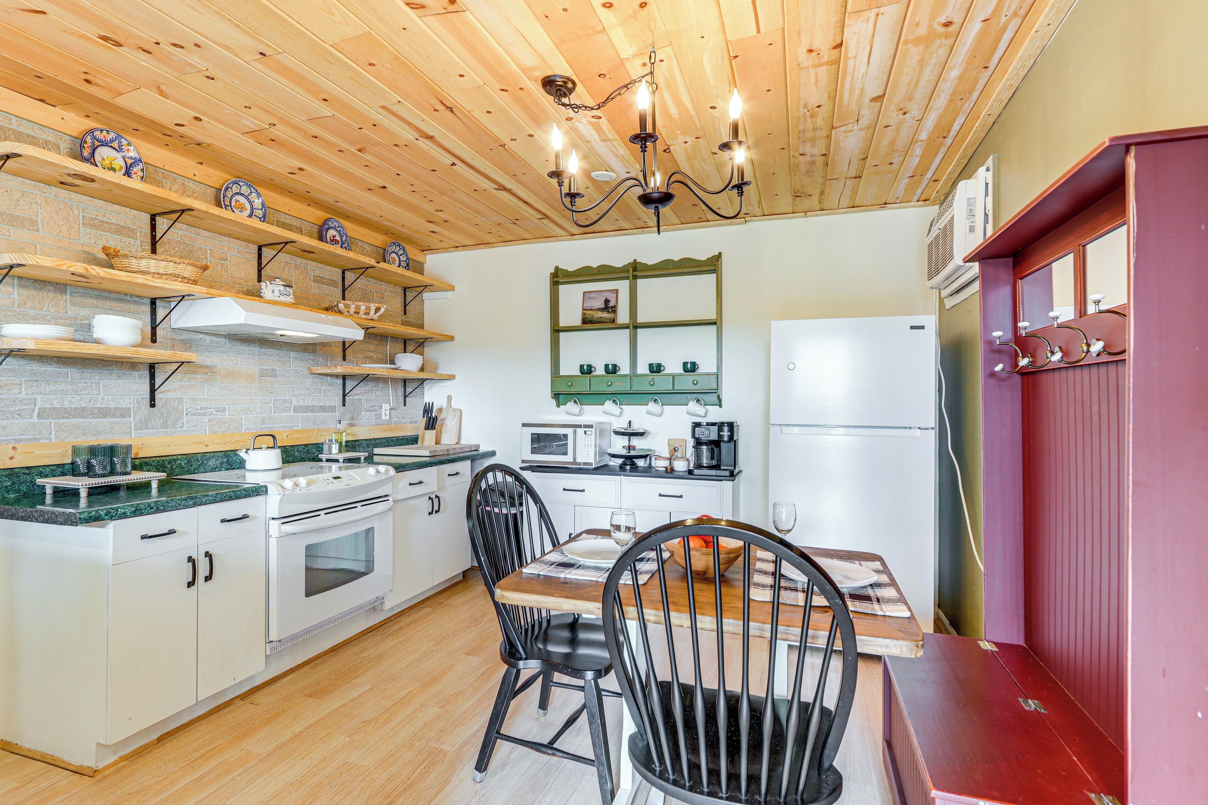 Una cocina con estantes de madera, estufa, sillas y una mesa de comedor.