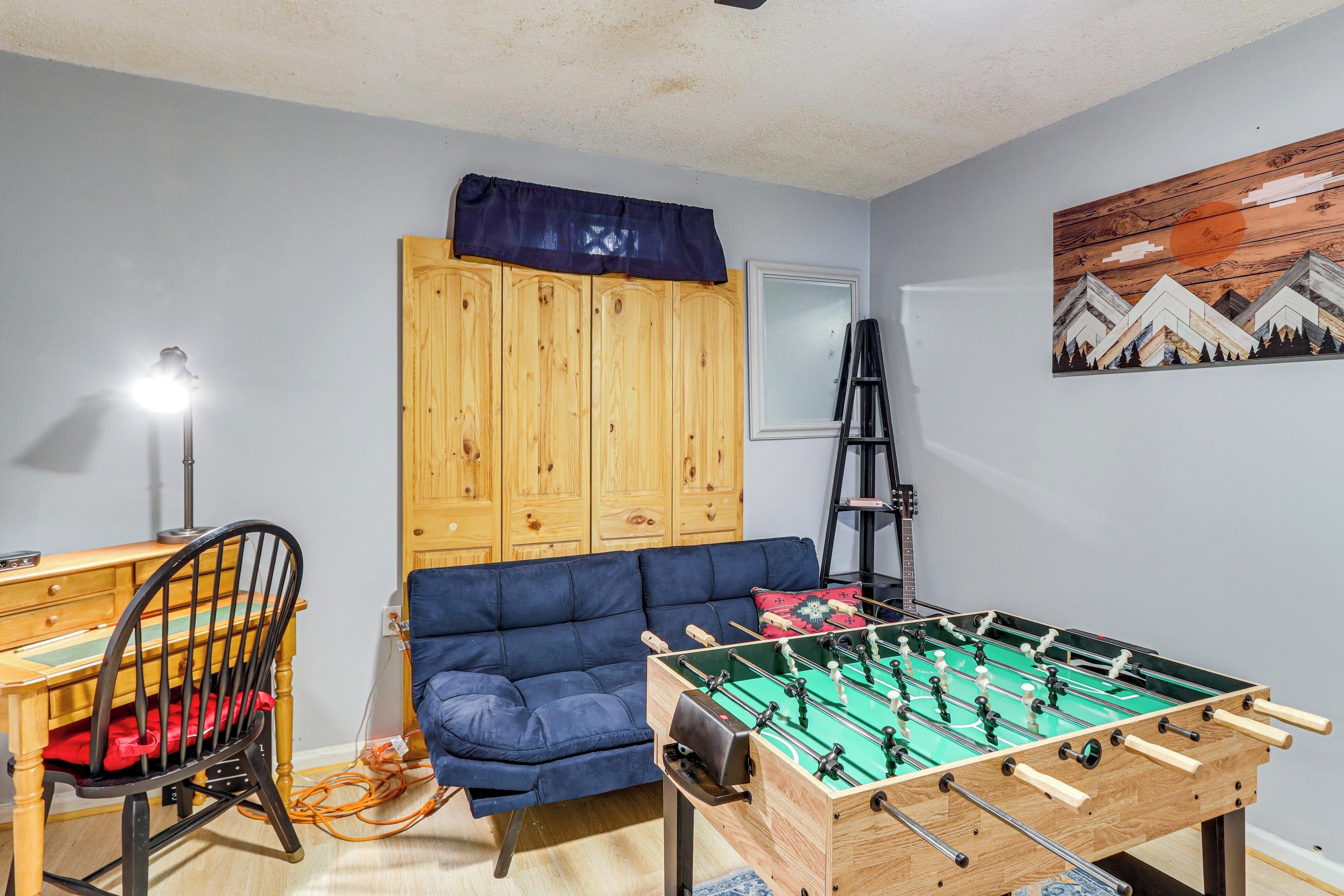 Una habitación con mesa de futbolín, un sofá azul, un mueble de madera y un cuadro en la pared.