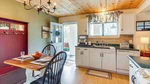 Una cocina con armarios de madera, una mesa de comedor con sillas, una araña y una ventana con cortinas.