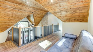 A spacious loft with exposed wooden beams, a stone fireplace, and a modern staircase with a glass railing. - New Build! Secluded Mountain Home in Murphy (Murphy)