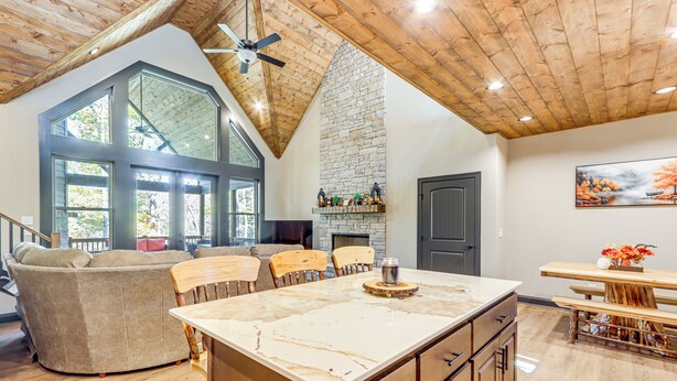 A spacious living area with a large island, wooden ceiling, and a stone fireplace. - New Build! Secluded Mountain Home in Murphy (Murphy)