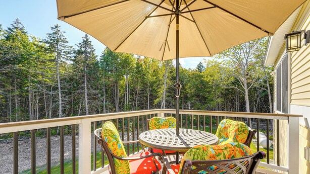 A deck with a table and chairs, a large umbrella, and a view of a forest.