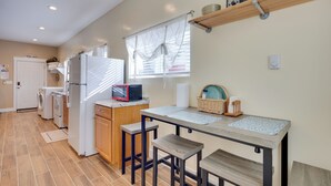 A compact kitchen with a refrigerator, microwave, and washing machine. There is a small dining table with stools and a window with curtains. - Cozy Couple's Retreat 5 Mi to Garden of the Gods! (Colorado Springs)