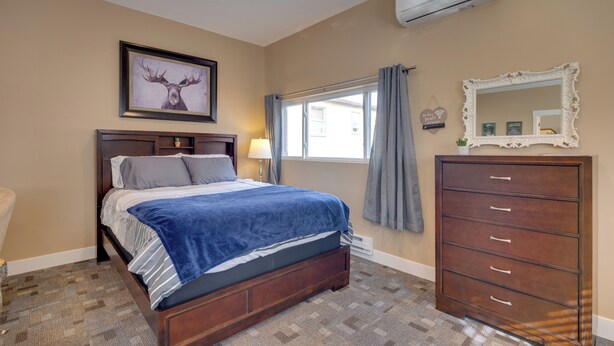 A bedroom with a bed, dresser, window with curtains, and a wall-mounted air conditioner. - Cozy Couple's Retreat 5 Mi to Garden of the Gods! (Colorado Springs)