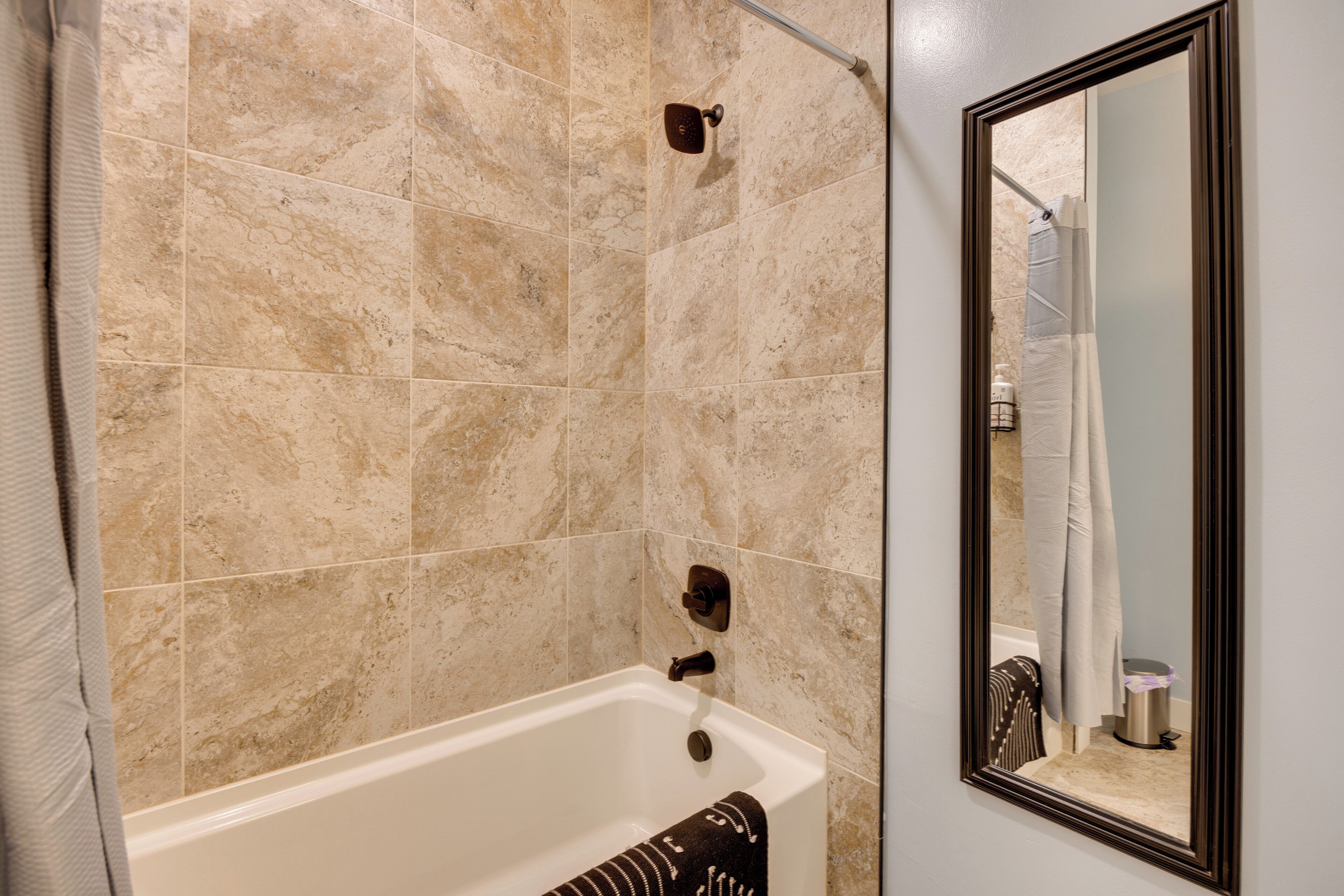 A bathroom with a bathtub, a shower curtain, and a mirror.