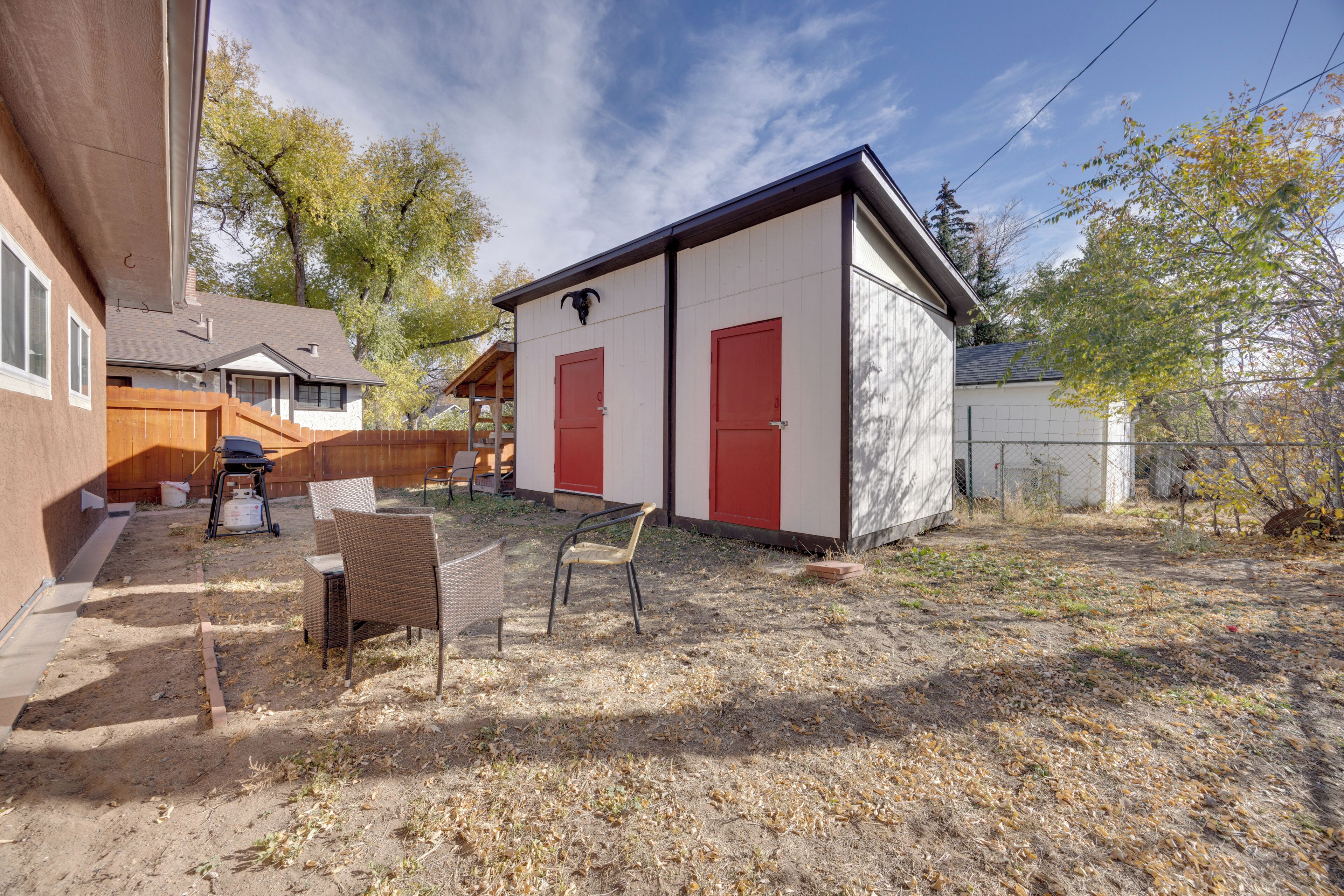 A small, single-story building with two red doors, a covered patio area with wicker furniture, and a fenced yard.