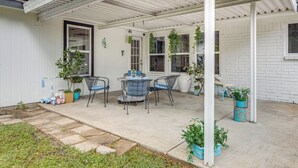 Une terrasse couverte avec une table et des chaises, des plantes en pot et un petit espace aménagé en jardin.