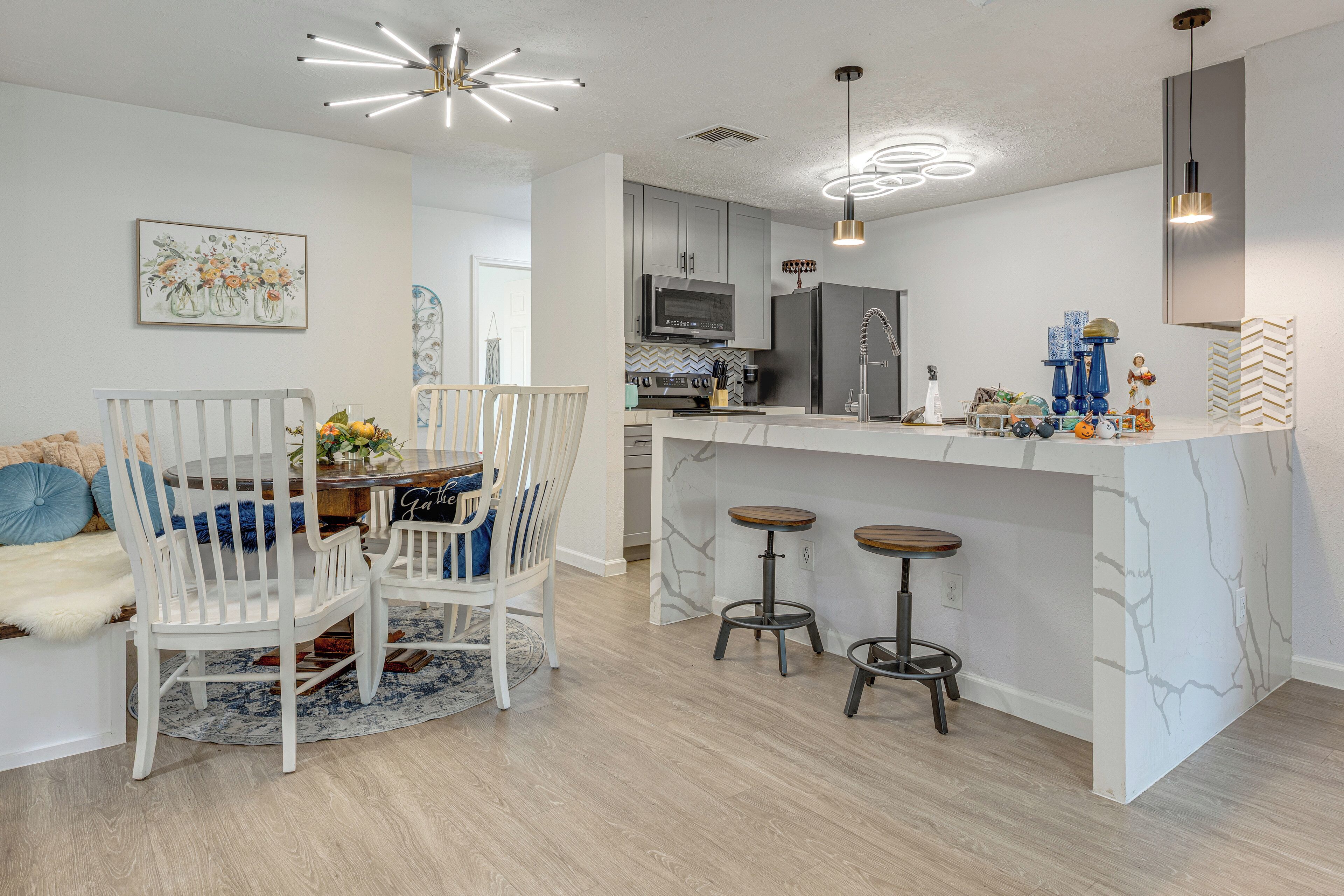 A modern kitchen with white cabinetry, a central island with stools, and pendant lighting.