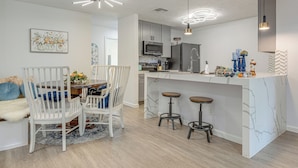 Une cuisine moderne avec des meubles blancs, un îlot central doté de tabourets et un éclairage suspendu.