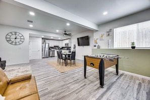 A modern living room with a foosball table, a dining area with a table and chairs, a kitchen in the background, and a large window with blinds. - 8 Mi to Usafa! Hot Tub Haven in Colorado Springs (Colorado Springs)