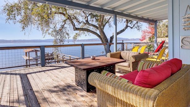 A covered deck with wicker furniture, a wooden table, and a view of the water. - Panoramic Views! Home w/ Boat Slip on Clear Lake (Lucerne)