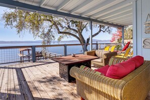 A covered deck with wicker furniture, a wooden table, and a view of the water. - Panoramic Views! Home w/ Boat Slip on Clear Lake (Lucerne)