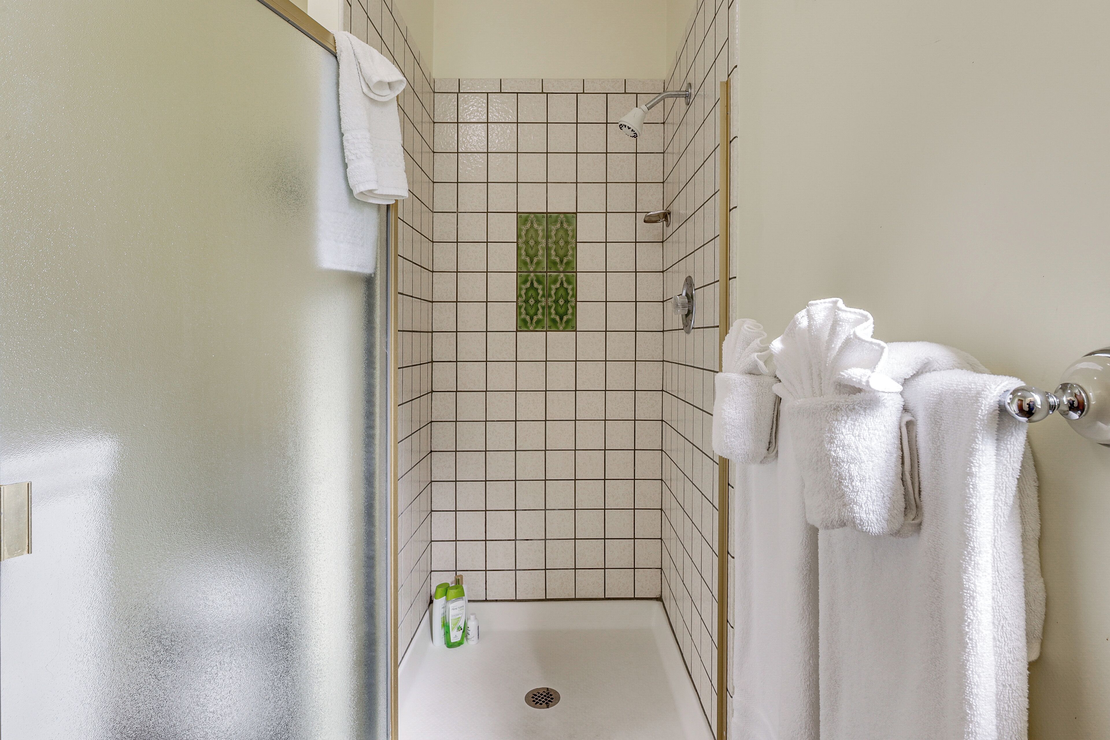 Eine Dusche mit einer Fliesenwand, einer grünen Dekofliese und einem weißen Handtuch, das an einem Haken hängt.