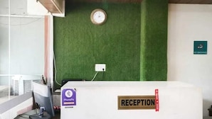 A reception area with a green wall, a clock, and a sign indicating no smoking. - Hotel Kuber 7 (Zirakpur)