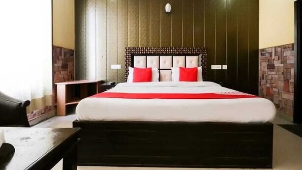 A hotel room with a large bed, a headboard with a patterned design, and a red accent pillow. - Hotel Kuber 7 (Zirakpur)