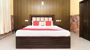 A large bed with a wooden headboard and red pillows, a white bedspread, and a red blanket. - Hotel Kuber 7 (Zirakpur)