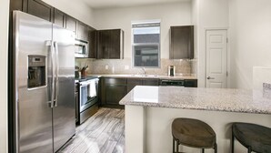 A modern kitchen with stainless steel appliances, granite countertops, and dark wooden cabinets. - Landing Apartments New Haven (New Haven)