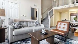 A living room with a grey sofa, a brown leather chair, a wooden coffee table, and a staircase leading to an upper level. - Landing Apartments New Haven (New Haven)