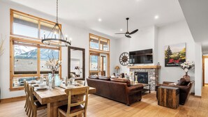 A spacious living area with a wooden dining table, leather sofas, and a fireplace. - Majestic Views! Tamarack Penthouse 3 BD / 3 BA (Canmore)