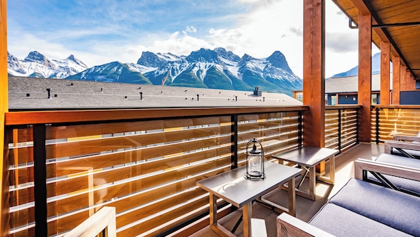 A wooden deck with tables and benches, overlooking snow-capped mountains. - Majestic Views! Tamarack Penthouse 3 BD / 3 BA (Canmore)