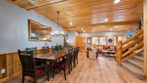 A spacious dining area with a wooden table and chairs, a chandelier, and a staircase leading to a loft. - Timberwolf Canyons Village, 3BR, sleeps 6, hot tub (Park City)