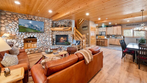 A cozy living room with a stone fireplace, leather sofa, and a dining area with wooden furniture. - Timberwolf Canyons Village, 3BR, sleeps 6, hot tub (Park City)