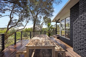 A wooden deck with a table and benches, surrounded by a black brick wall and large windows. - Treetop Views: 3  BR, 1  BA House in Rye, Sleeps 8 (Rye)