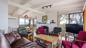 Uma sala de estar ampla com sofá de couro, duas poltronas, mesa de centro de madeira e lareira.
