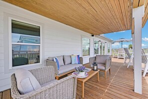 Une terrasse extérieure couverte, aménagée avec des meubles en osier, une table en bois et offrant une vue sur l’océan.