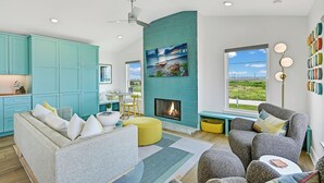 Una sala de estar moderna con muebles de color aguamarina, chimenea y un amplio ventanal con vistas al exterior.