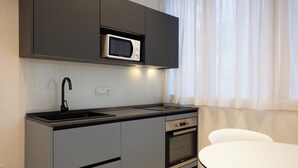 A modern kitchen with a built-in microwave, a sink, and an oven. There is a white table and a chair in the dining area. - Luxury Freedom Juno (Palermo)