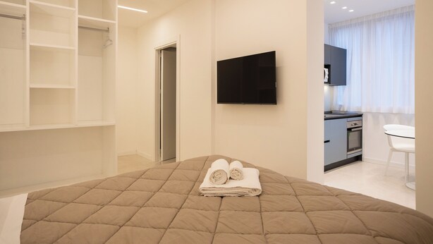A modern hotel room with a large bed, a TV mounted on the wall, a kitchenette, and a walk-in closet. - Luxury Freedom Juno (Palermo)