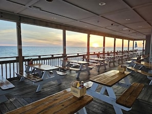 An outdoor dining area with wooden tables and benches, overlooking the sea. - The Grove Holly 113 - 1 Bedroom - Lazy River - Seascape Resort (Miramar Beach)