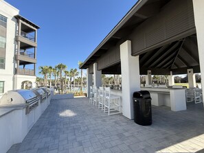An outdoor patio area with barbecue grills, white chairs, and a trash can. - The Grove Juniper 247 - 1 Bedroom - Lazy River - Seascape Resort (Miramar Beach)