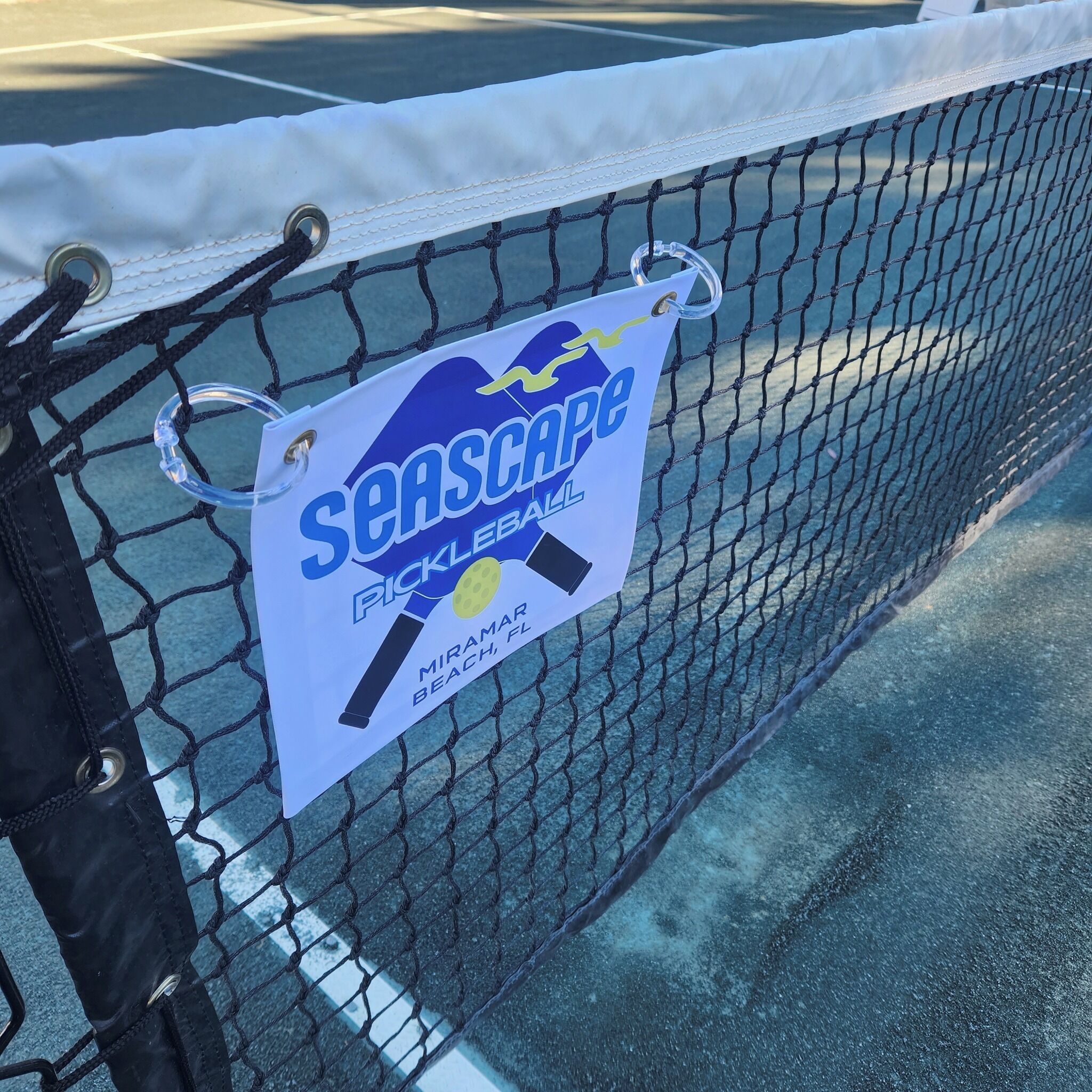 Un recinto cubierto con malla que muestra un letrero que dice 'Seascape Pickleball' y menciona 'Miramar Beach, FL'.