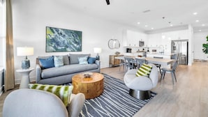 Een moderne woonkamer met een bank, fauteuils, een salontafel en een eethoek, met een keuken op de achtergrond.