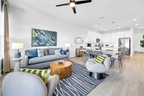 A modern living room with a sofa, armchairs, a coffee table, and a dining area with a kitchen in the background. - The Grove Juniper 243 - 2 Bedrooms - Lazy River - Seascape Resort (Miramar Beach)