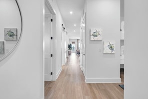 A hallway with white walls and wooden flooring, featuring several framed artworks on the walls. - The Grove Juniper 243 - 2 Bedrooms - Lazy River - Seascape Resort (Miramar Beach)