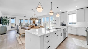 A modern kitchen with white cabinetry, a central island, pendant lighting, and a view of the outdoors through large windows.