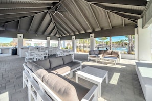 Un patio exterior con mobiliario blanco, incluyendo sofás y mesas, bajo una estructura cubierta.